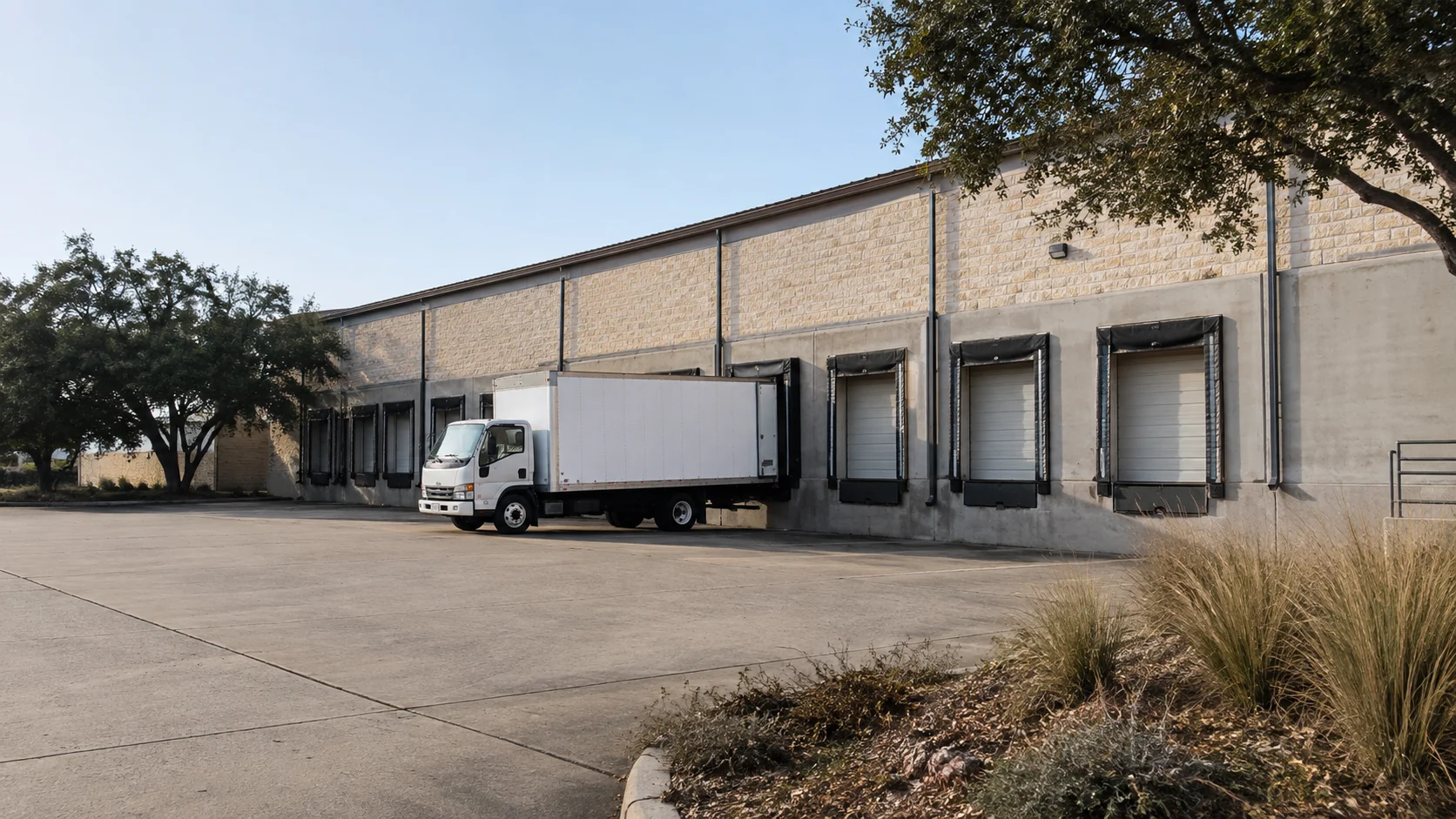 Illustrative view of one white box truck beside a row of loading bays in a Central Texas setting